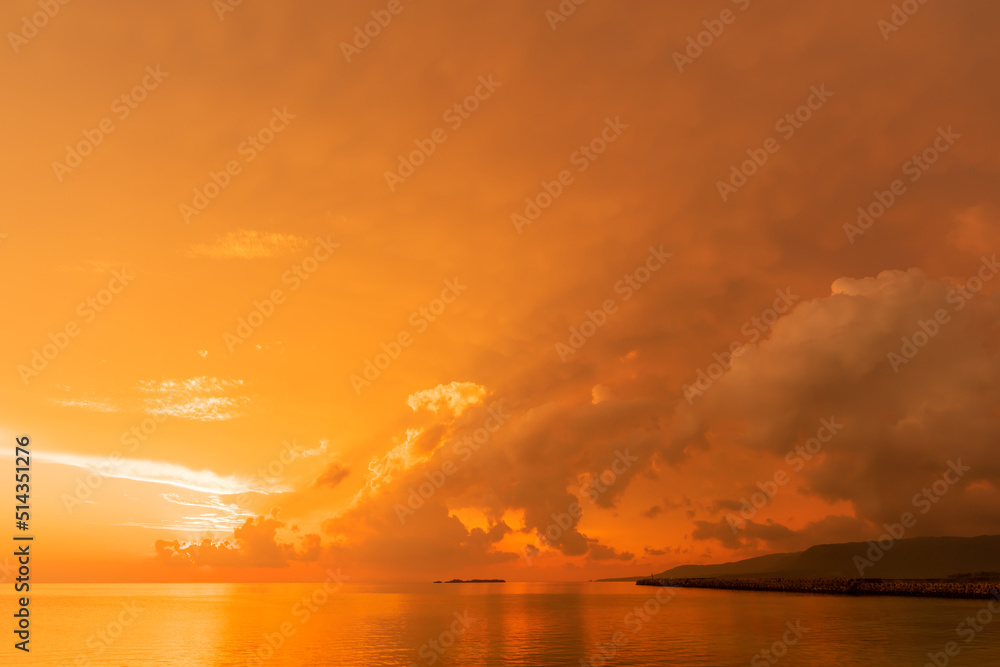 Vibrant sunrise in yellow orange, sun lighting colorful clouds over entire sky at seashore.
