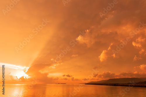 Amazing bright sunrise in yellow orange sky, sunbeams over colorful clouds at seashore.