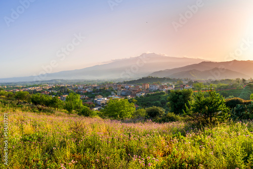 picturesque highland landscape with amazing view from hill with golden grass and green bushes to a valley town with majectic mountains and scenic cloudy sunset on background © Yaroslav