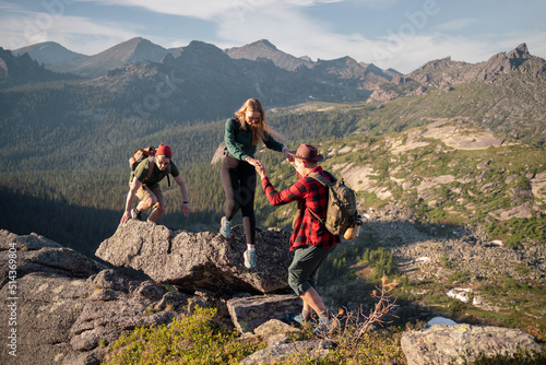 Group of young tourists two guys and girl with backpacks in mountains go along route