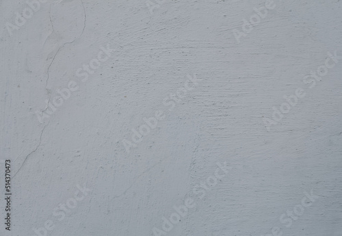 An old cement painted wall, white grey abstract background. A scratched concrete wall texture with cracks.