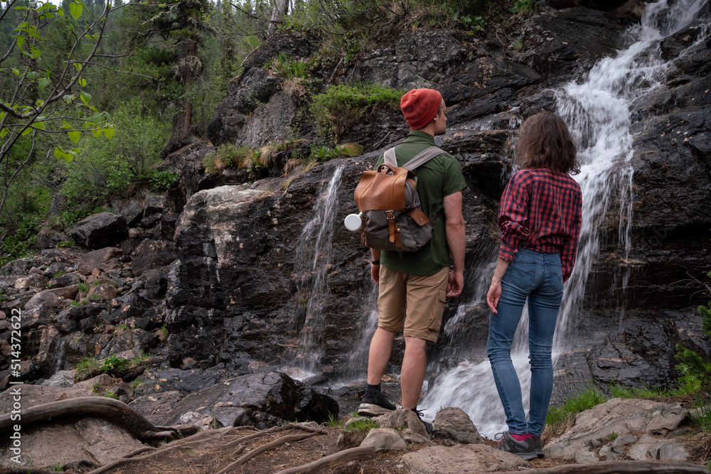 Young tourists adventurers girl and guy on background of waterfall in forest