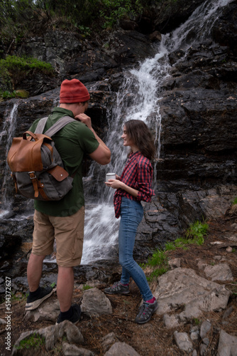 Young tourists adventurers girl and guy on background of waterfall in forest
