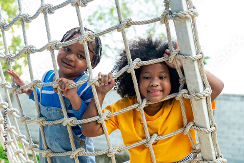 Little African boy and girl friends playing and climbing rope net together at playground in the park on summer vacation. Children kid enjoy outdoor activity playing and learning at school playground