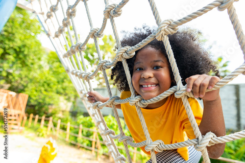 Canvas Print Happy Little African child girl playing and climbing rope net at outdoor playground in the park on summer vacation