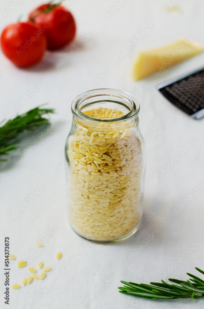 Raw Italian risoni pasta in a glass jar with ingredients on a table. The concept of traditional cuisine. Vertical orientation. Raw Italian risoni pasta in a glass jar with ingredients on a table. The concept of traditional cuisine. Vertical orientation.