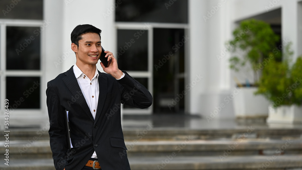Positive young businessman talking on mobile phone while walking down on the stairs of an office building