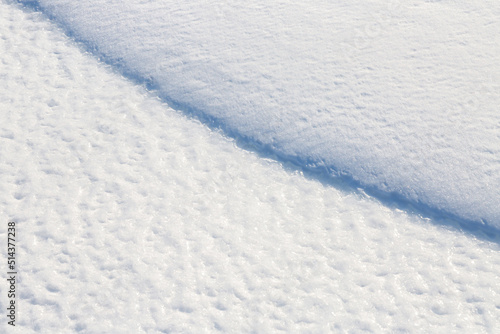 Beautiful winter background with snowy ground. Natural snow texture. Wind sculpted patterns on snow surface. Closeup top view with copy space.