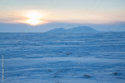 Winter arctic landscape. View of the snow-covered tundra and snow-capped mountains. Cold frosty winter weather. Endless Arctic Desert. Northern nature of the polar region. Sunset. Chukotka, Russia.