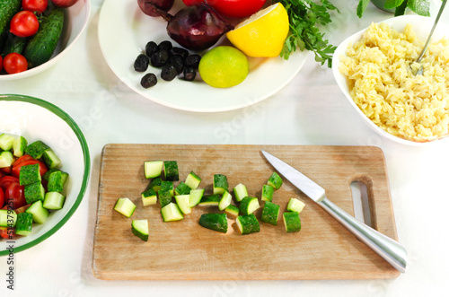 Sliced cucumber slices on a wooden cutting board. The process of preparing Orzo salad with ingredients on the table. The concept of vegetarian food. Horizontal orientation.
