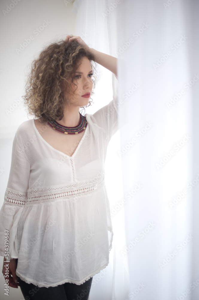 Slim young fashion model with curly hair wearing white blouse in a frame of window. Picture of lovely sexy fashionable woman with sunglasses and necklace Slim young fashion model with curly hair wearing white blouse in a frame of window. Picture of lovely sexy fashionable woman with sunglasses and necklace
