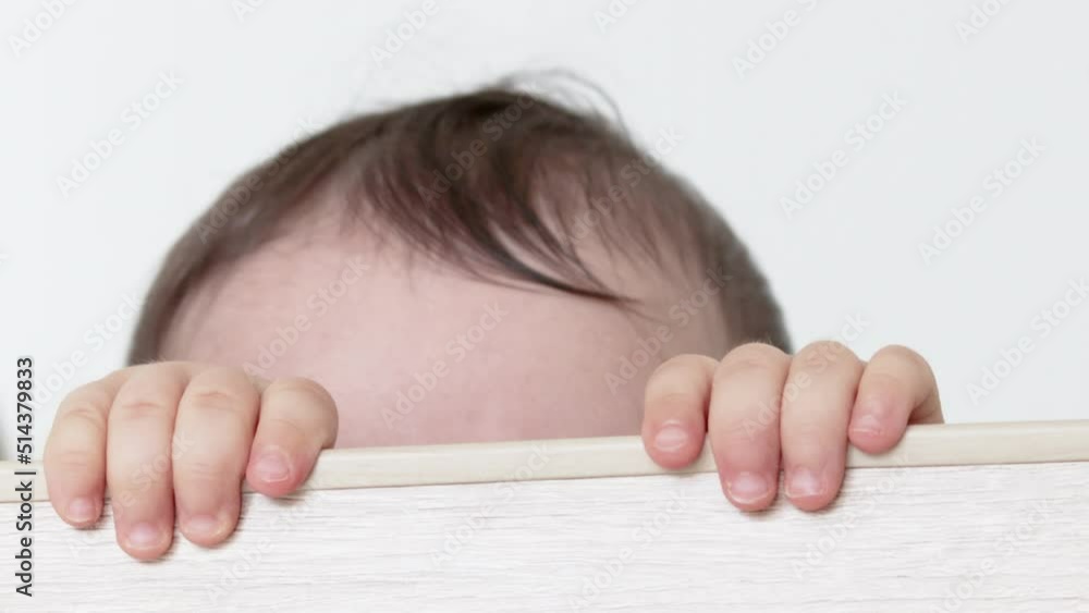 cute little baby boy is crying in the crib, holding the wooden bars