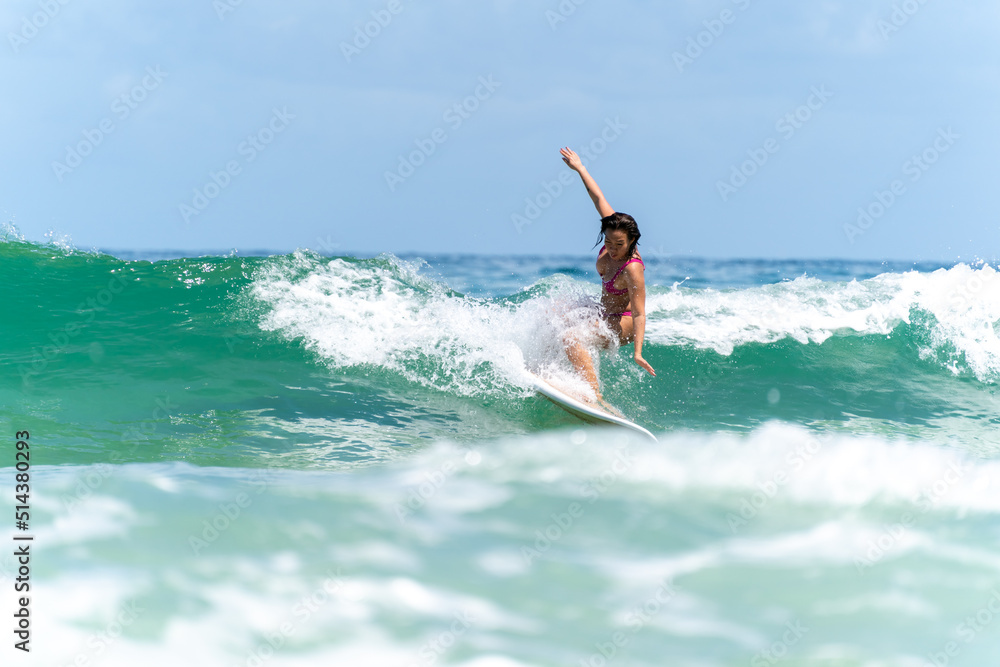 Asian woman surfer surfing and riding surfboard the wave in the sea at tropical beach in sunny day. Healthy female enjoy outdoor activity lifestyle and water sport exercise surfing on summer vacation Asian woman surfer surfing and riding surfboard the wave in the sea at tropical beach in sunny day. Healthy female enjoy outdoor activity lifestyle and water sport exercise surfing on summer vacation