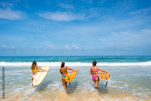  Group of Asian woman surfer in swimwear holding surfboard walking together on tropical beach in sunny day. Female friends enjoy outdoor activity lifestyle water sport surfing on summer vacation