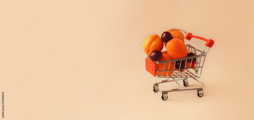 Fresh cherries and apricots in shopping cart on beige background. Online shopping minimalistic concept. . Black Fridays sales banner. Healthy, organic, vegan food