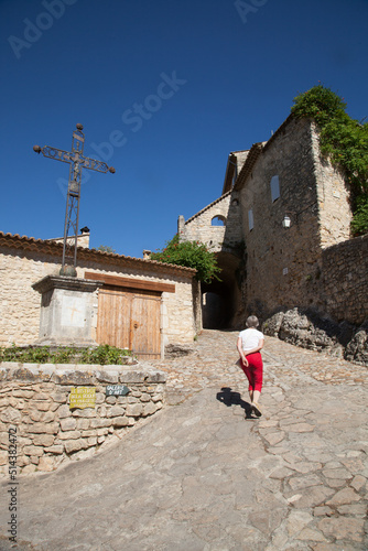 Touriste femme montant une ruelle du village touristique de la Roque sur Cèze et passant au pied d'une croix métallique