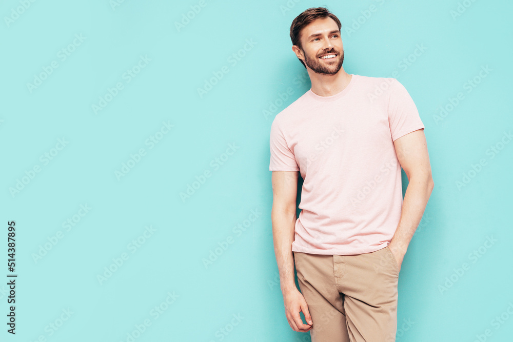 Portrait of handsome smiling stylish hipster lambersexual model. Sexy man dressed in pink T-shirt and trousers. Fashion male isolated on blue wall in studio Portrait of handsome smiling stylish hipster lambersexual model. Sexy man dressed in pink T-shirt and trousers. Fashion male isolated on blue wall in studio