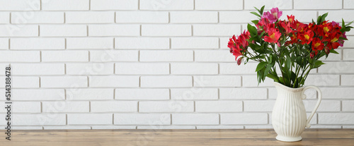 Vase with bouquet of beautiful alstroemeria flowers on table near light brick wall. Banner for design