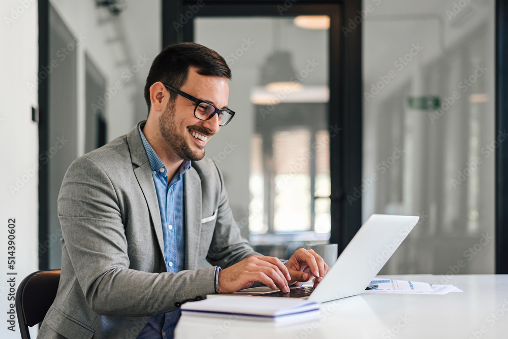 Smiling young entrepreneur typing on laptop while working at office desk Smiling young entrepreneur typing on laptop while working at office desk