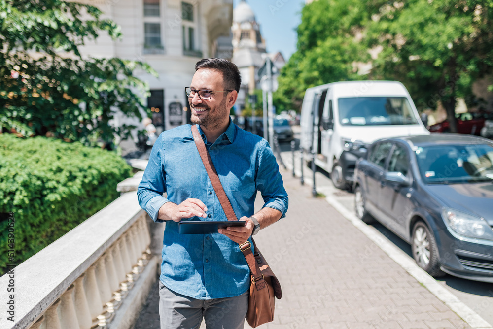 Obraz premium Happy executive using digital tablet while walking on sidewalk during sunny day