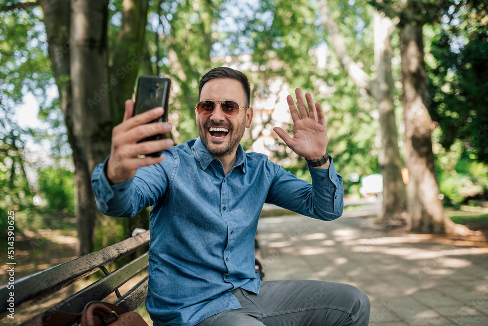 Cheerful male professional waving while video calling on smart phone at the park Cheerful male professional waving while video calling on smart phone at the park