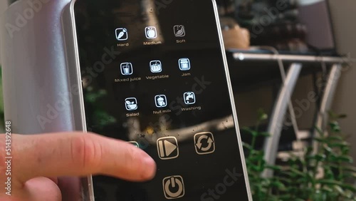 A human finger presses on the juicer's touch screen.