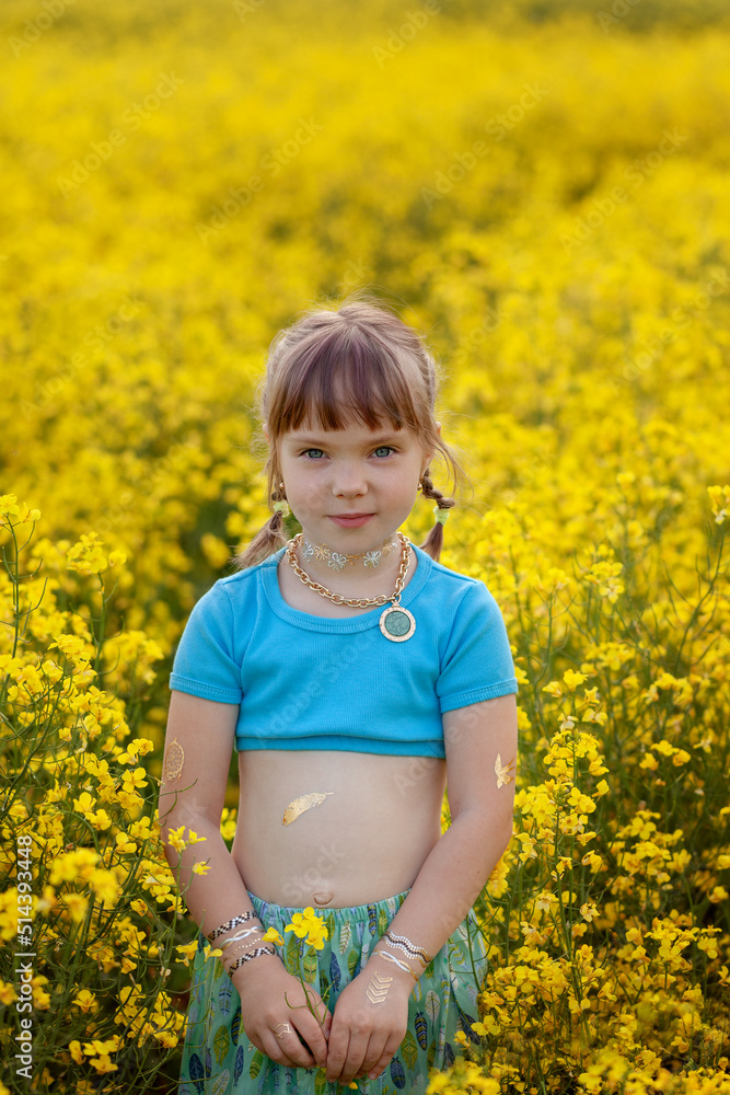 Pretty little girl walking with blue dress in boho style in rapeseed field. Cute young lady model in summer sunny day. Pretty little girl walking with blue dress in boho style in rapeseed field. Cute young lady model in summer sunny day.