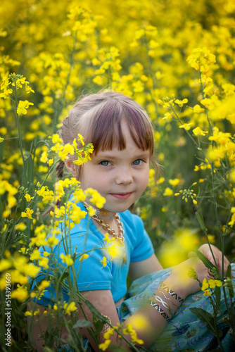 Portrait of a cute girl kid in a yellow rape flower field. A child in a blooming meadow. Authenticity, rural life, eco-friendly
