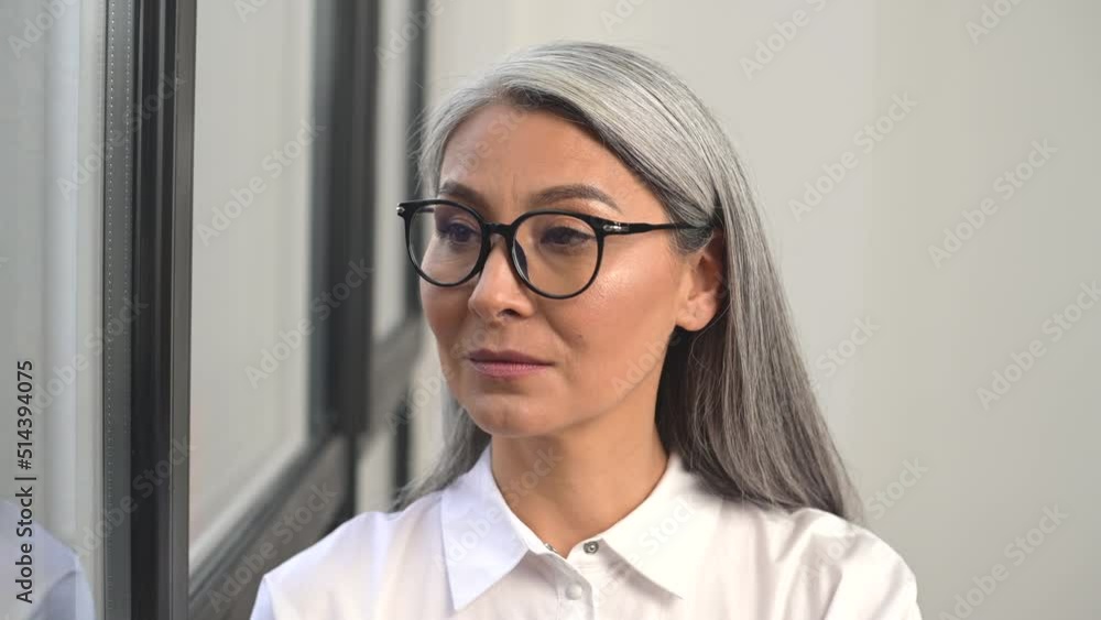 Portrait of positive charismatic Asian businesswoman in white shirt and glasses smiling to camera standing in modern office, high-skilled lidder Portrait of positive charismatic Asian businesswoman in white shirt and glasses smiling to camera standing in modern office, high-skilled lidder