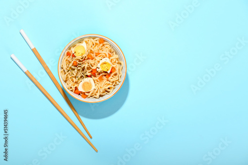 Bowl of tasty noodles with eggs on blue background