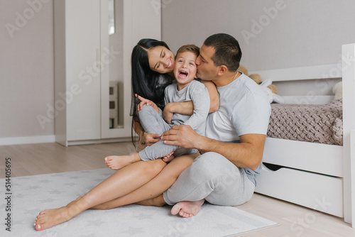 Young happy parents kiss their five-year-old son on the cheeks while sitting on the floor in the nursery