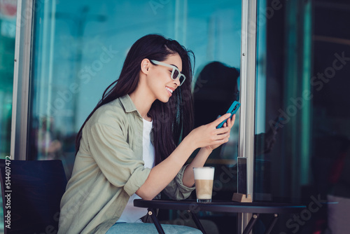 Photo of cute sweet lady dressed casual clothes dark eyewear sitting cafeteria chatting modern gadget outside urban town house