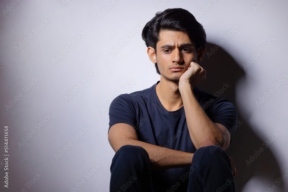 Portrait of a sad teenage boy with hand on chin sitting lonely at home Portrait of a sad teenage boy with hand on chin sitting lonely at home