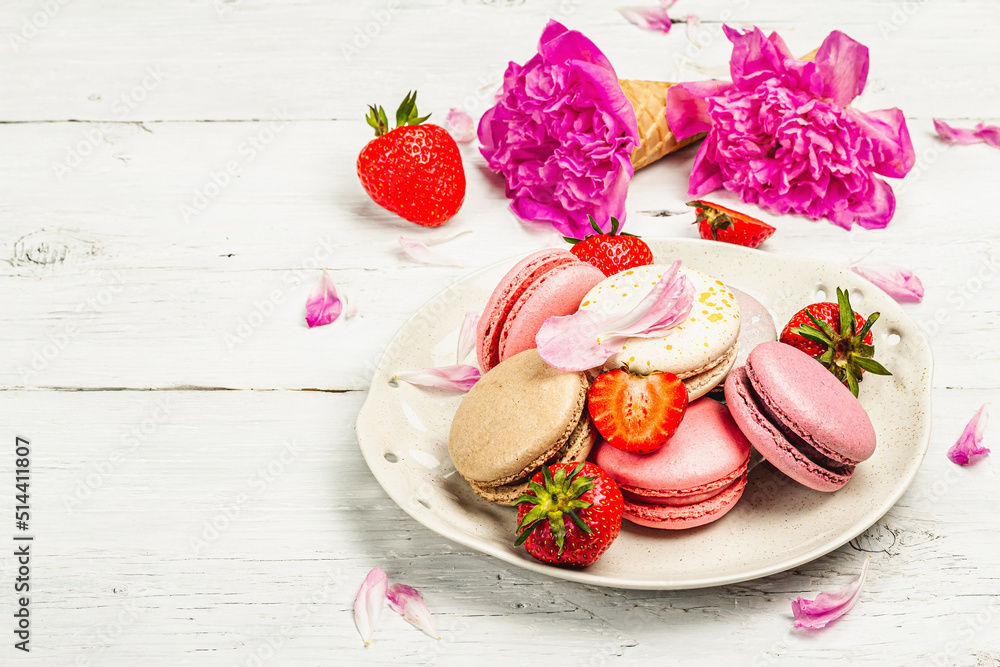 Macarons with strawberries and peonies flower petals, on a white wooden background