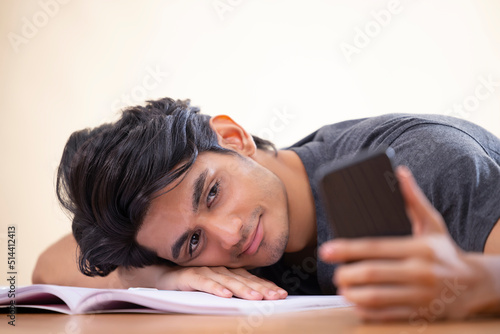 Close-up portrait of a tired teenager leaning head on hand with holding a smartphone