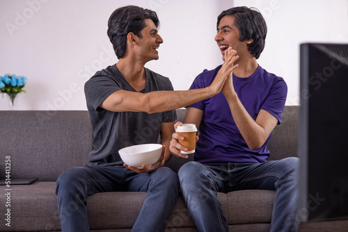Two excited teenage boys high-fiving while watching TV in living room