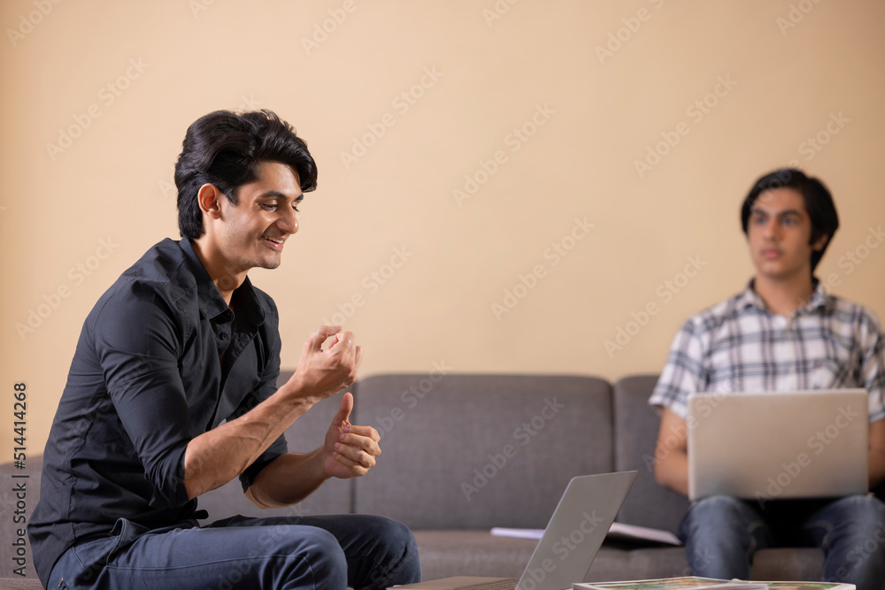 Two happy teenage boys doing homework at home using laptop Two happy teenage boys doing homework at home using laptop