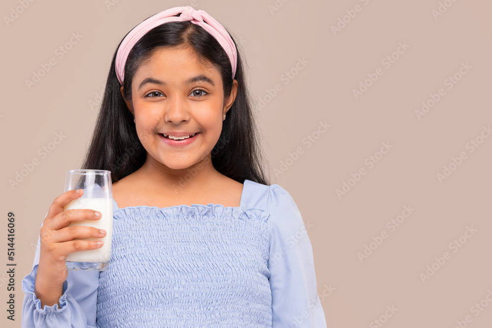 Portrait of cheerful little girl holding a glass of milk against plain background Portrait of cheerful little girl holding a glass of milk against plain background