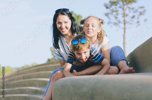Happy family lifestyle and holiday concept. Mother, little boy, girl sitting, walking in old city, street. laughing on a summer sunny day. Having fun © Oleksandra