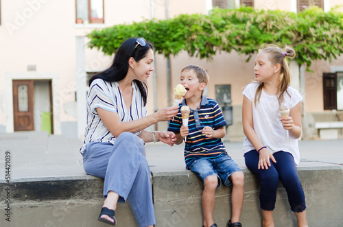 Happy family lifestyle and holiday concept. Mother, little boy, girl sitting, eating ice cream in old city, street. laughing on a summer sunny day. Having fun. Staying cool
