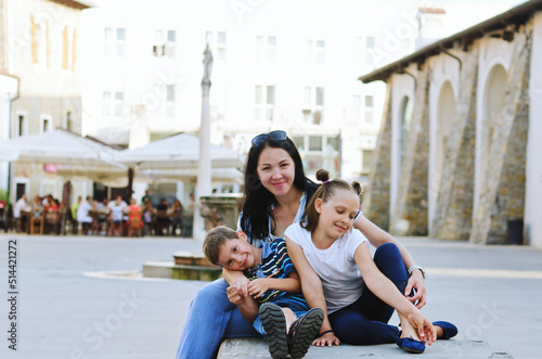 Happy family lifestyle and holiday concept. Mother  little boy  girl sitting  walking in old city  street. laughing on a summer sunny day. Having fun