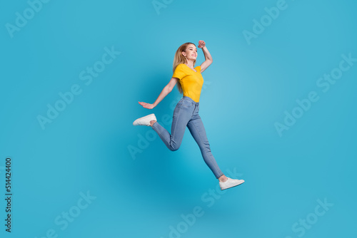 Portrait of sportive active girl in motion jumping over in the air isolated on blue background having looking empty space