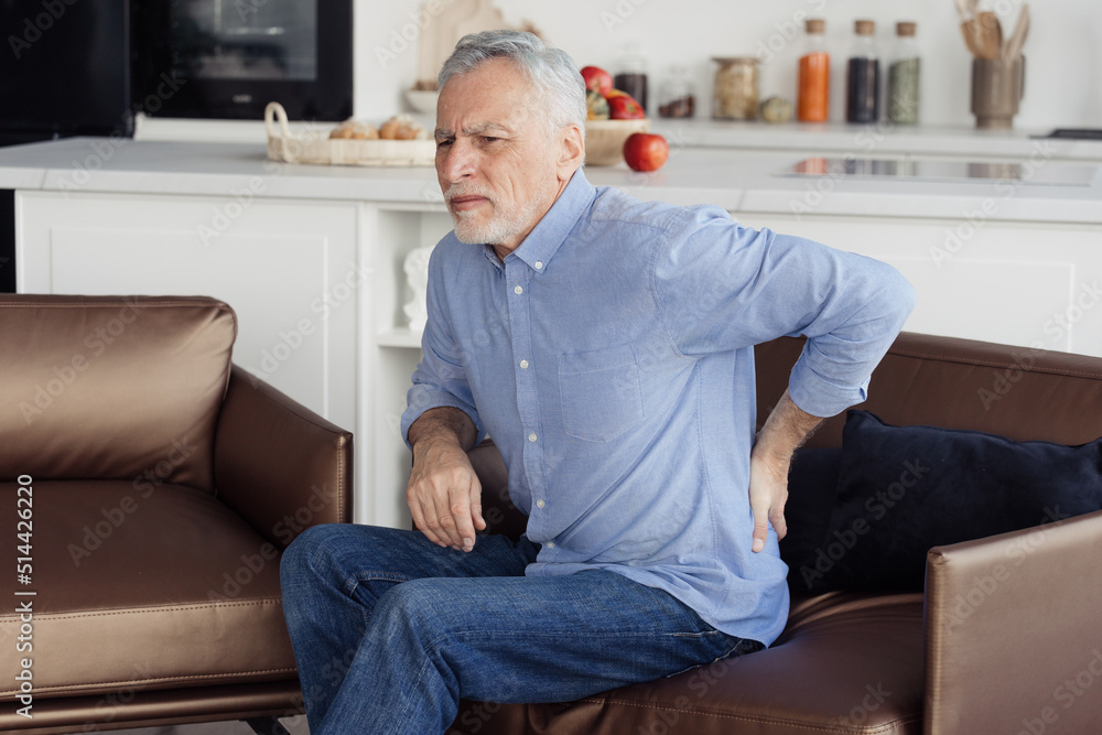 Senior man feeling lower back pain, sitting on armchair