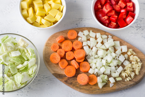 Chopped ingredients for a vegetable dish: potatoes, cabbage, carrots, onions, garlic, tomatoes on a light blue background. Cooking delicious vegan food