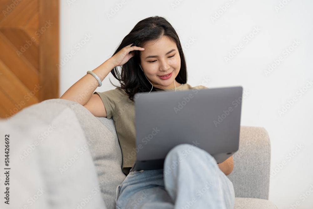 young asian woman laying in living room on sofa studying with headphones and computer, stay at home concept young asian woman laying in living room on sofa studying with headphones and computer, stay at home concept