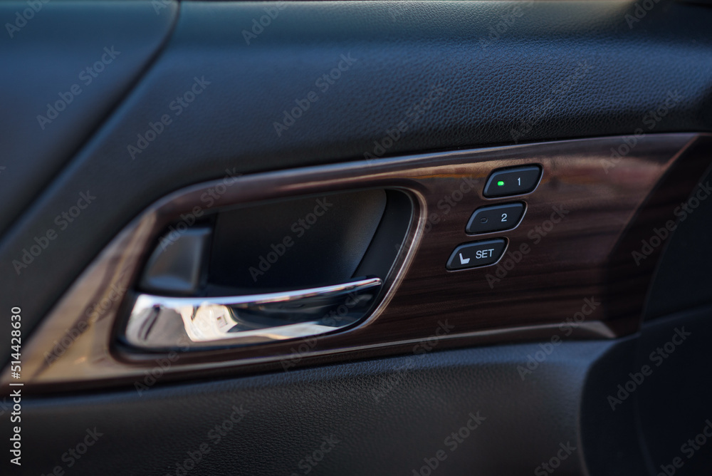 Car inside door chrome handle. Door trim. Black and brown new car interior. Clean door leather and panel. Left Panel with seat settings drivers. Buttons to adjust the driver's seat memory. Closeup.