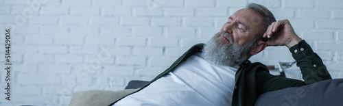 Fotografie upset senior man with beard suffering crisis while sitting on couch in living room, banner