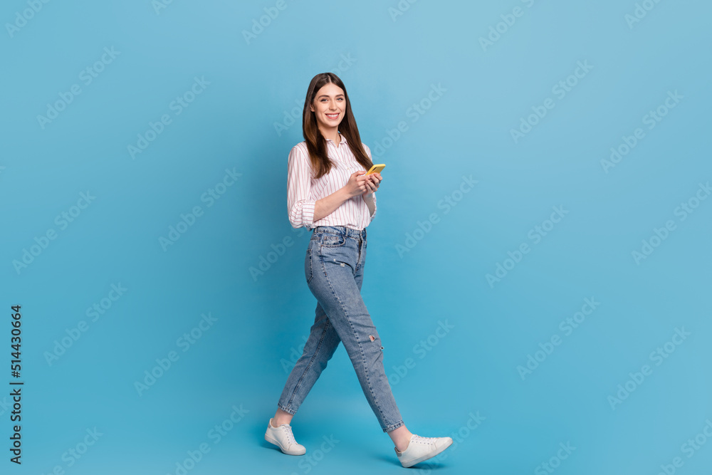Full length body size view of attractive cheerful trendy girl using gadget strolling isolated over bright blue color background Full length body size view of attractive cheerful trendy girl using gadget strolling isolated over bright blue color background