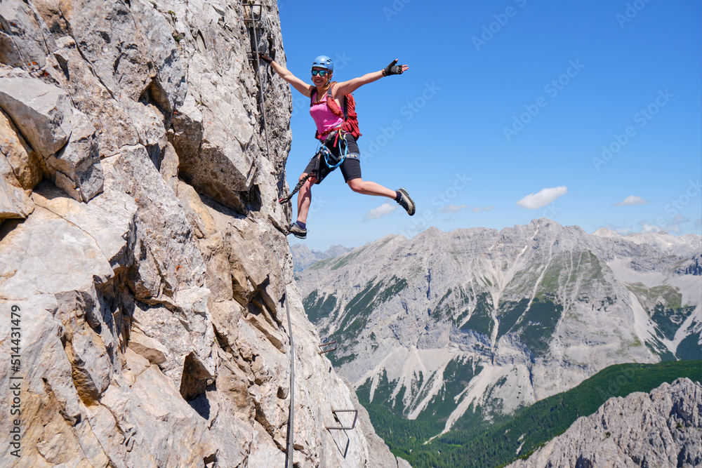 Happy active woman hangs out on via ferrata Nordkette Innsbruck, Austria. Exposed rock route, adventure, activity, tourism, klettersteig.