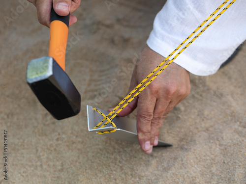 Hand of man holding a rubber mallet,hammering aluminium steel tent stakes pegs nail,fastening tent for camping,hit or beat anchor of the tent into the ground,hammer with rubber head, wooden handle